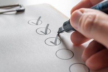 Das Bild zeigt eine Hand mit einem Kugelschreiber, die eine Checkliste ausfüllt.