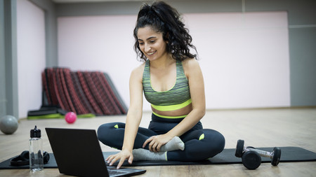 Online-Sportkurs Das Bild zeigt eine junge Frau auf einer Sportmatte, die online an einem Sportkurs teilnimmt