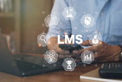 Das Bild zeigt einen Mann vor einem Laptop, der auf dem Handy tippt. In der Mitte des Bildes ist das Wort "LMS" zu lesen und ein Kreis aus acht Icons zu sehen, die die Funktionen des LMS darstellen.